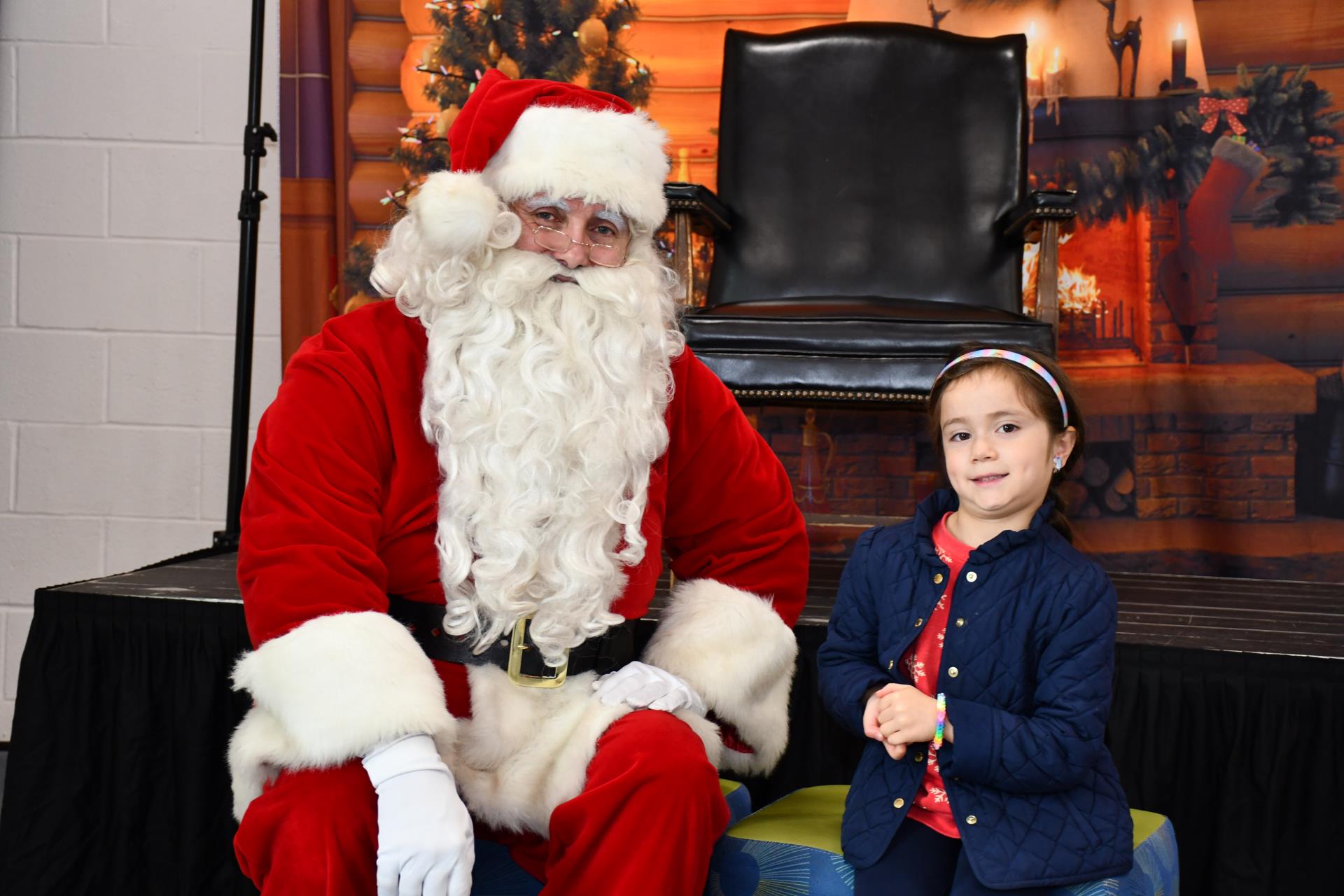 Santa sits next to a kid who stands and poses with a silly smile. Taken at the 2023 Cookies with Santa event at the Vienna Community Center.